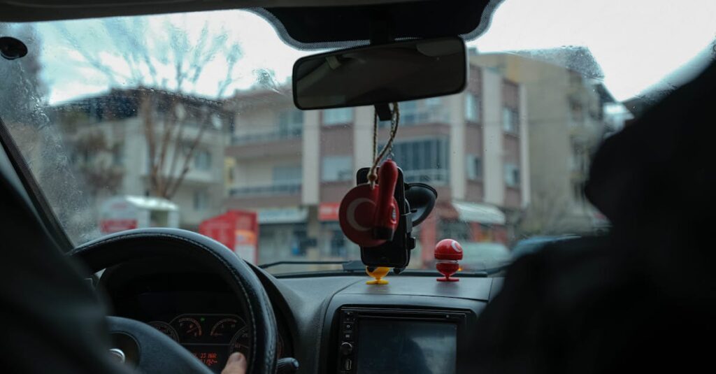 A driver's perspective of a car interior navigating through city streets with focus on the dashboard and rearview mirror.
