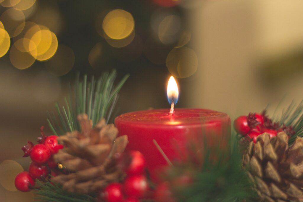 Red candle with pine cones and blurred bokeh lights, perfect for holiday decor inspiration. Scented holiday candle burning in cozy room — post about fragrance sensitivity and MCS